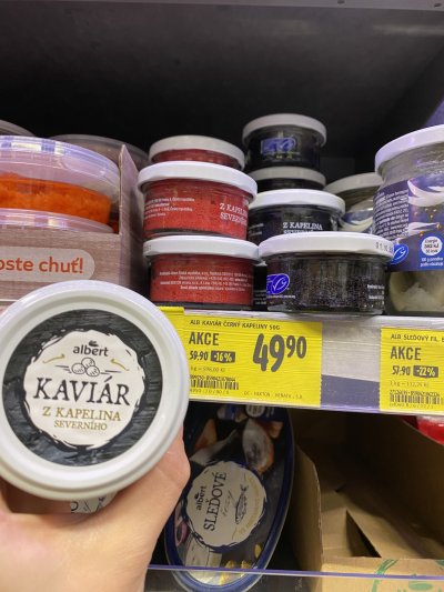 Ruka držící produkt Albert Kaviár z kapelina severního před regálem supermarketu