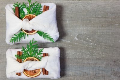 Dva dárky zabalené v látce a ozdobené větvičkami, celou skořicí a sušenými plátky pomeranče