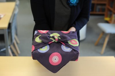 Žena drží v rukou dárek zabalený do čtvercového šátku