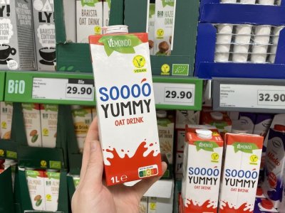 Ruka držící balení ovesného mléka před regálem supermarketu