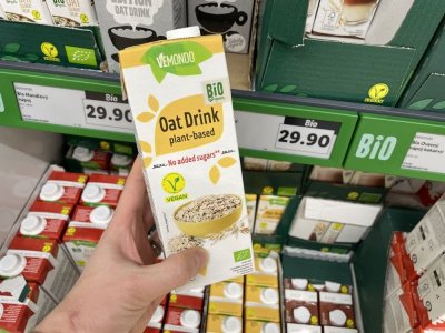 Ruka držící balení ovesného mléka před regálem supermarketu