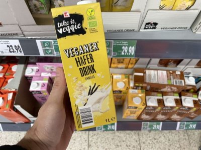 Ruka držící balení rostlinného mléka před regálem supermarketu