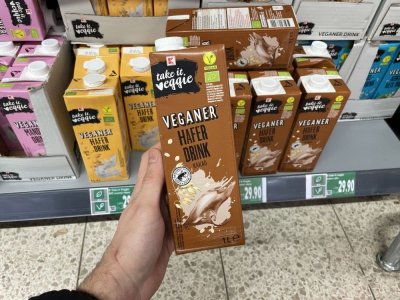 Ruka držící balení rostlinného mléka před regálem supermarketu