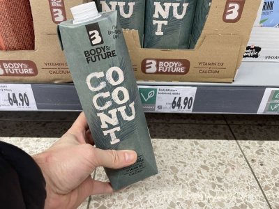 Ruka držící balení kokosového mléka před regálem supermarketu