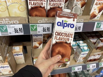 Ruka držící balení rostlinného mléka před regálem supermarketu