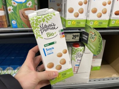 Ruka držící balení sójového mléka před regálem supermarketu