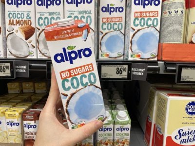 Ruka držící balení kokosového mléka před regálem supermarketu