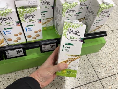 Ruka držící balení rýžového mléka před regálem supermarketu