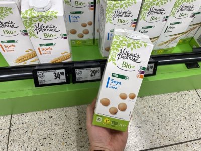 Ruka držící balení sójového mléka před regálem supermarketu