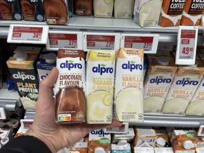 Ruka držící tři balení rostlinného mléka před regálem supermarketu