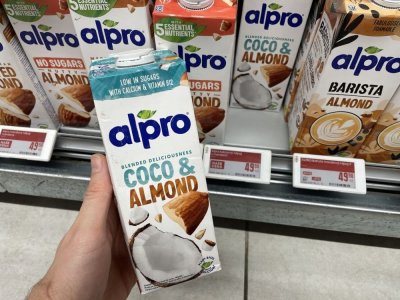 Ruka držící balení rostlinného mléka před regálem supermarketu