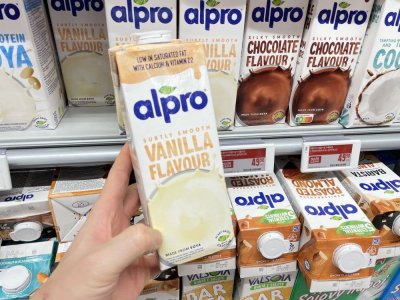 Ruka držící balení rostlinného mléka před regálem supermarketu