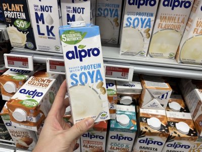 Ruka držící balení rostlinného mléka před regálem supermarketu