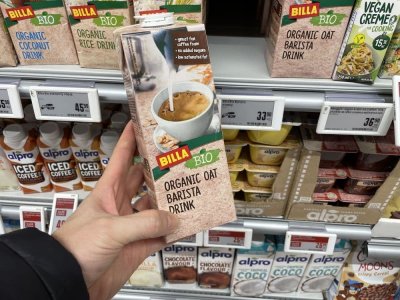 Ruka držící balení rostlinného mléka před regálem supermarketu