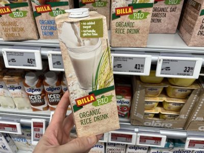 Ruka držící balení rostlinného mléka před regálem supermarketu