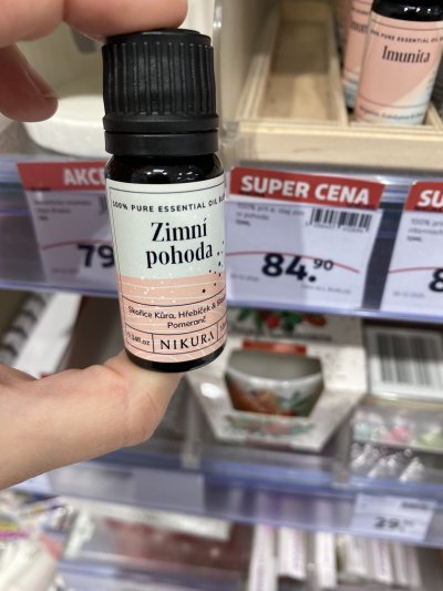 Ruka držící vonný olej před regálem drogerie