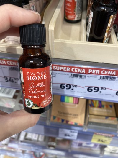 Ruka držící vonný olej před regálem drogerie