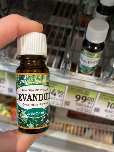 Ruka držící vonný olej před regálem drogerie