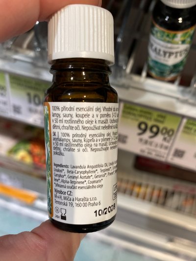 Ruka držící vonný olej před regálem drogerie