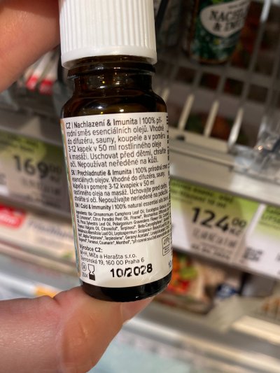 Ruka držící vonný olej před regálem drogerie