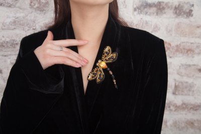 Žena v černém kabátu s výraznou zlatou broží ve tvaru vážky