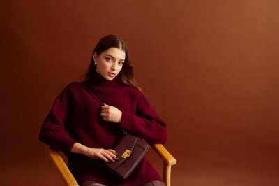 Žena ve vínovém svetru s hnědou kabelkou