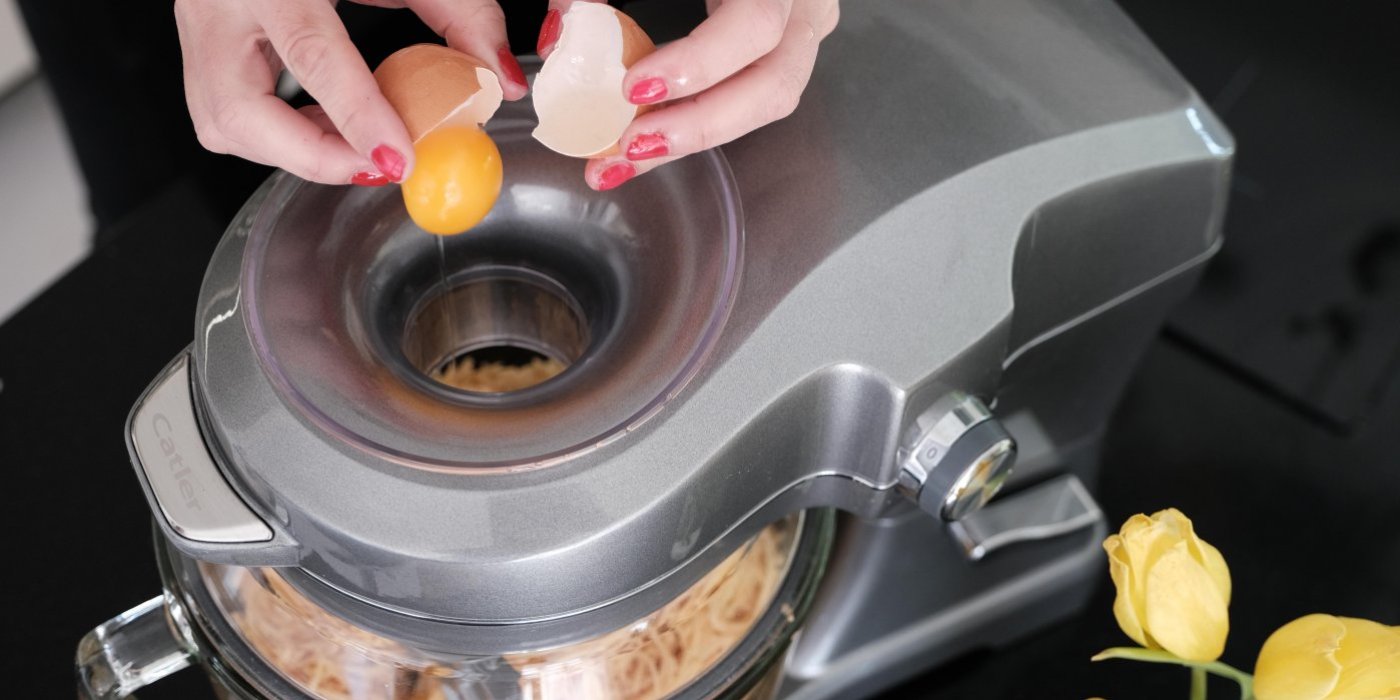 Žena rozklepává vejce do kuchyňského robotu s těstem na bramboráky