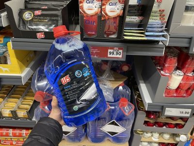 Ruka držící kanystr zimní směsi do ostřikovačů před regálem supermarketu