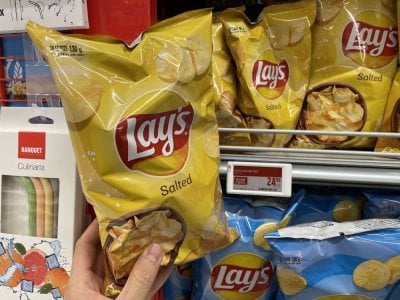 Ruka držící solené brambůrky před regálem v supermarketu