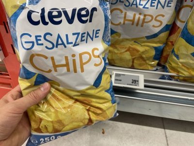 Ruka držící solené brambůrky před regálem v supermarketu