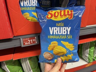Ruka držící solené vroubkované brambůrky před regálem v supermarketu