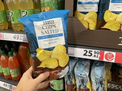 Ruka držící solené brambůrky před regálem v supermarketu