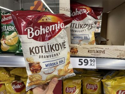 Ruka držící solené brambůrky před regálem v supermarketu