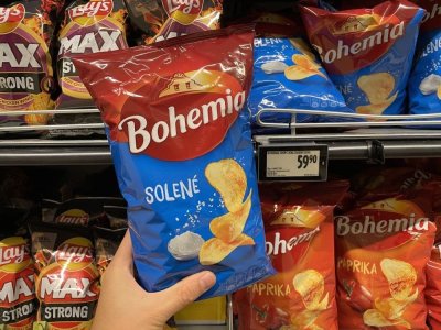 Ruka držící solené brambůrky před regálem v supermarketu