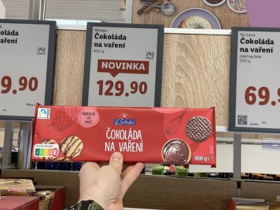 Ruka držící tabulkovou čokoládu před regálem supermarketu