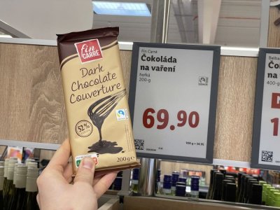 Ruka držící tabulkovou čokoládu před regálem supermarketu