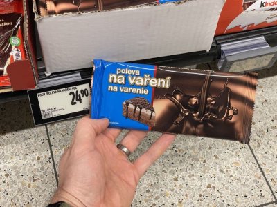 Ruka držící tabulkovou čokoládu před regálem supermarketu