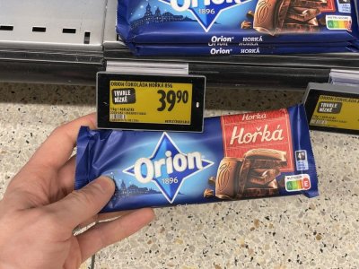 Ruka držící tabulkovou čokoládu před regálem supermarketu