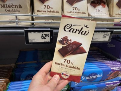 Ruka držící tabulkovou čokoládu před regálem supermarketu