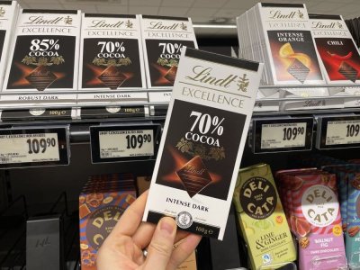 Ruka držící tabulkovou čokoládu před regálem supermarketu