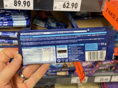 Ruka držící tabulkovou čokoládu před regálem supermarketu