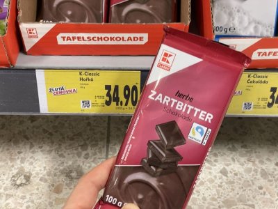 Ruka držící tabulkovou čokoládu před regálem supermarketu