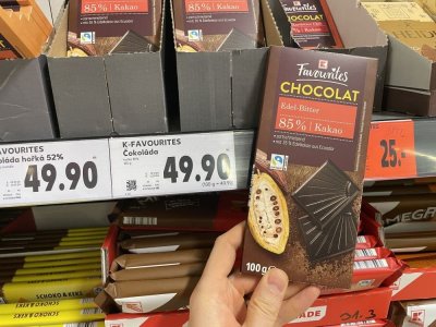 Ruka držící tabulkovou čokoládu před regálem supermarketu
