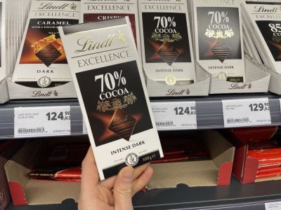 Ruka držící tabulkovou čokoládu před regálem supermarketu