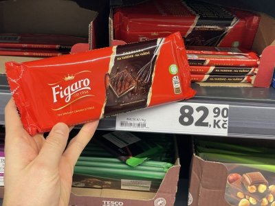 Ruka držící tabulkovou čokoládu před regálem supermarketu