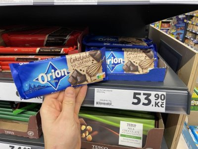 Ruka držící tabulkovou čokoládu před regálem supermarketu