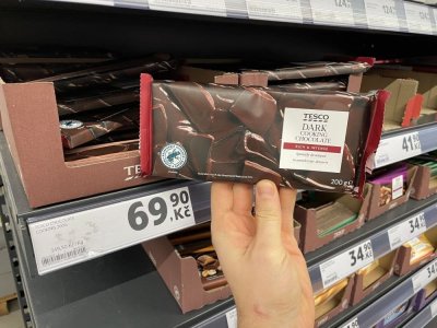 Ruka držící tabulkovou čokoládu před regálem supermarketu