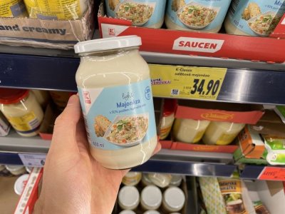 Ruka držící majonézu před regálem supermarketu
