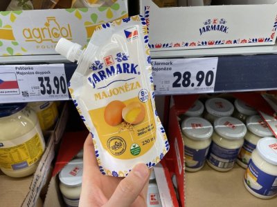 Ruka držící majonézu před regálem supermarketu