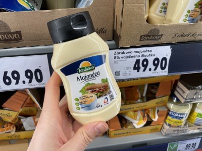Ruka držící majonézu před regálem supermarketu